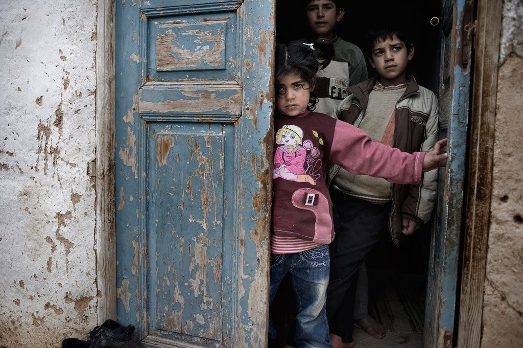 Crianças sírias abrigadas na entrada de uma casa, em meio a tiros e bombardeios, em uma cidade afetada pelo conflito. Foto: UNICEF/ Alessio Romenzi